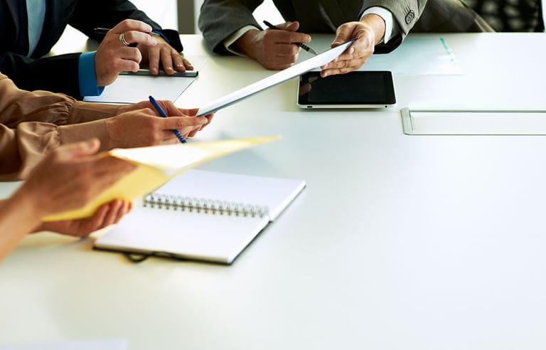 View of people's hands and notes on conference room table.