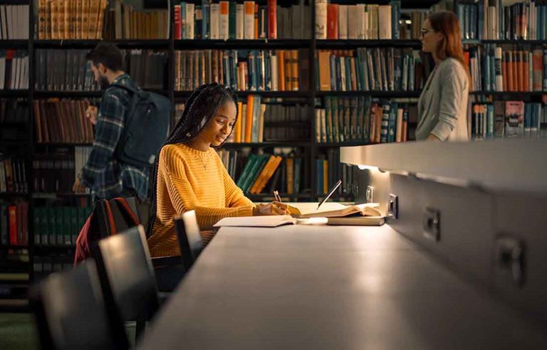 Student sitting at a desk in a library doing homework.