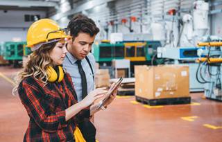 Factory worker & businessperson going over inventory in manufacturing facility.
