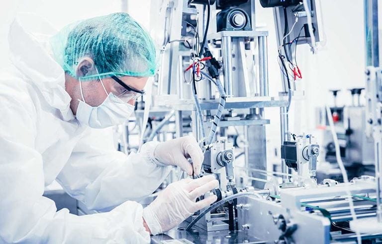 Scientist in a mask and hazmat suit working with a machine.