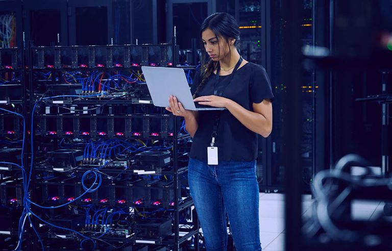 Cybersecurity professional on their laptop in a server room.