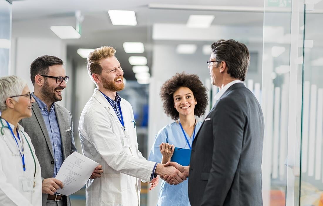 Happy medical professionals shake hands with a business professional at a medical facility