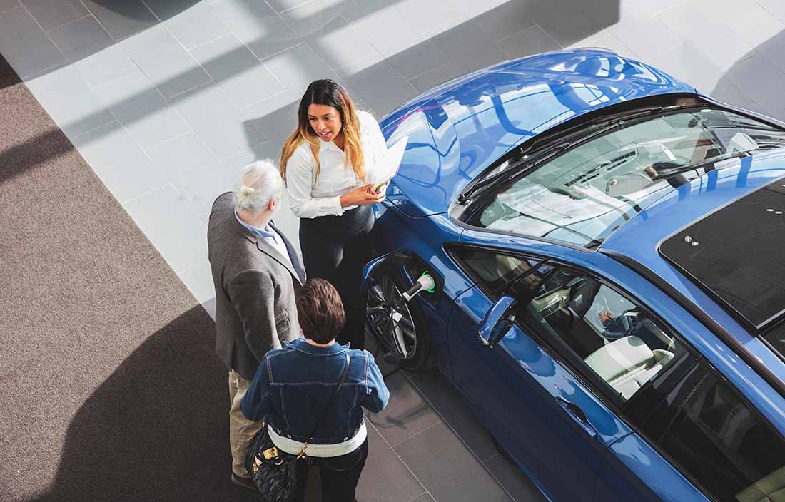 Car salesman talking to a couple at a car dealership.