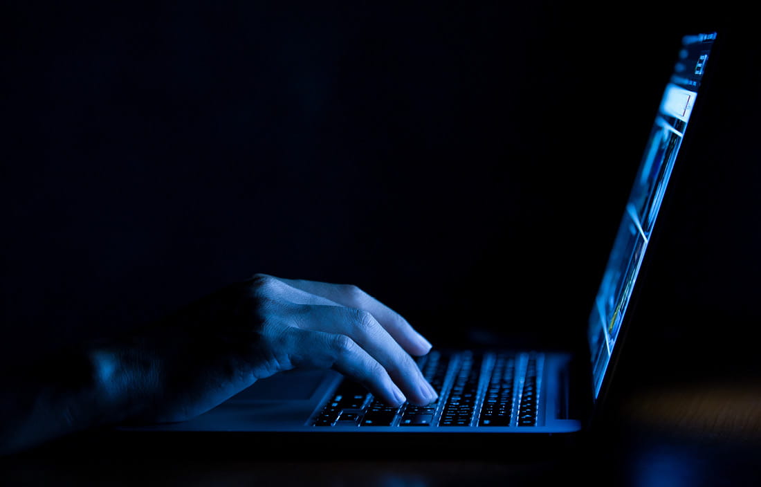 Person searching on their computer in a dimly lit room.