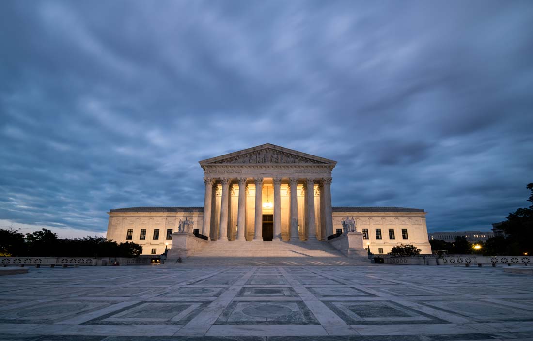 U.S. Supreme Court building lit up against a stormy night sky.