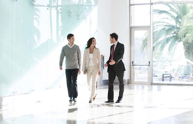 Three business professionals walking in an open, modern office lobby.