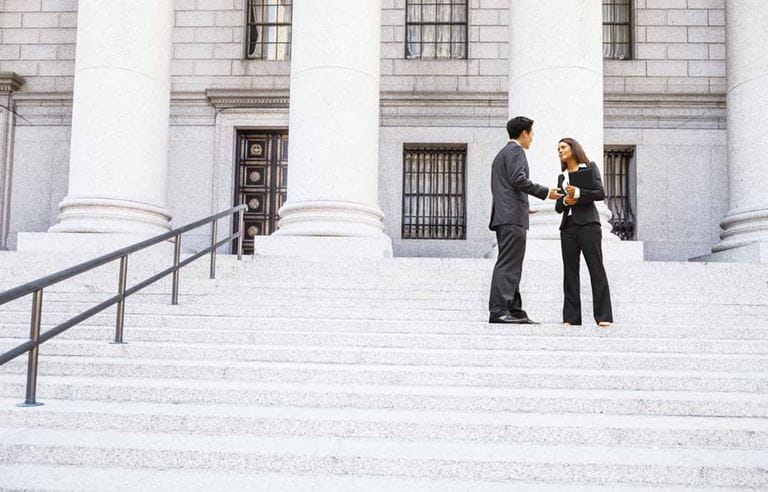 Two tax professionals shaking hands and talking on the steps of a government building.