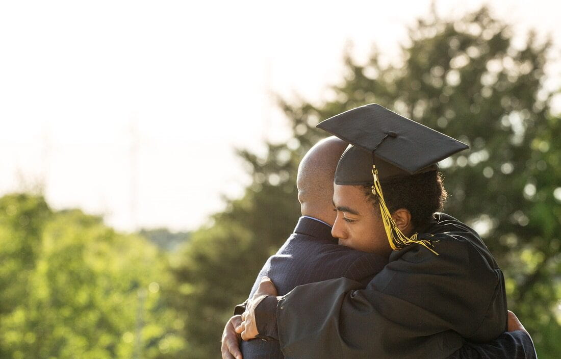 High school graduate in a cap and gown hugging their parent.