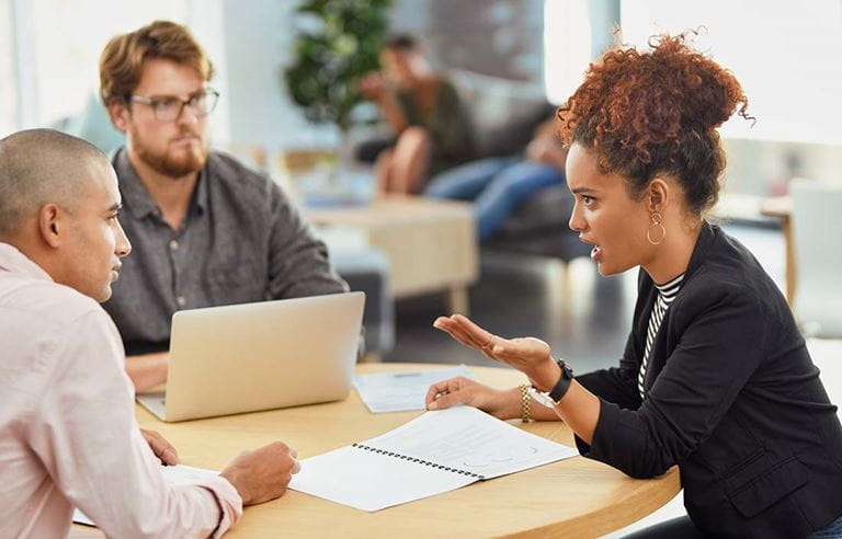 Three business professionals having a conversation at a circular table while sitting down