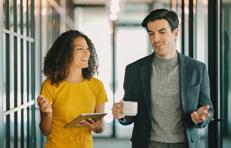 Two benefit plan professionals talking to each other in an office hallway.