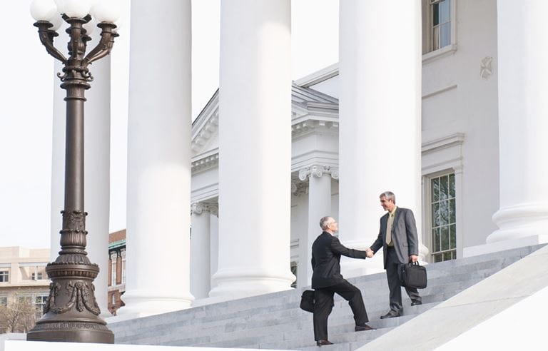 Two tax professionals shaking handing on the steps of a government building.