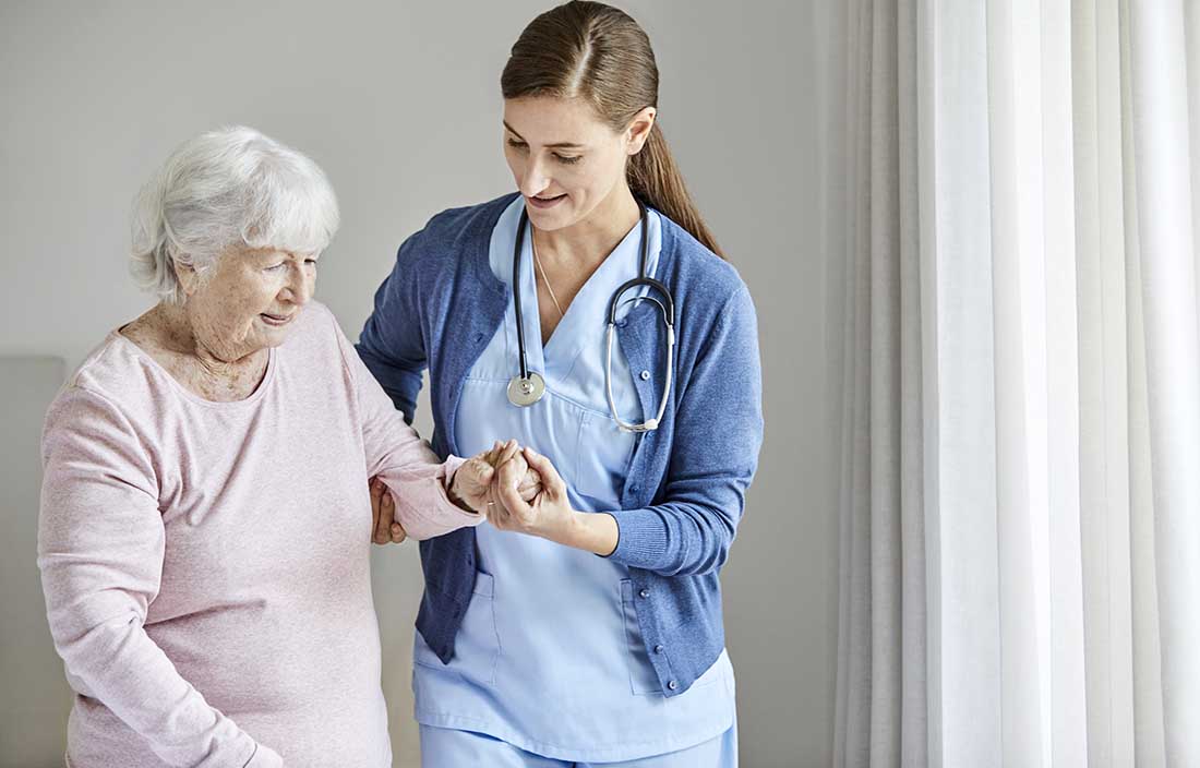 Nurse helping senior citizen walk across the room.