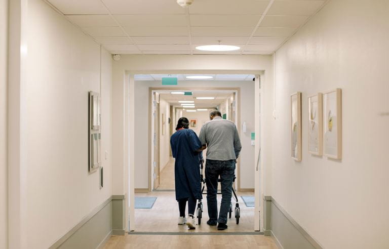 Senior care professional walking with a patient down the hallway.