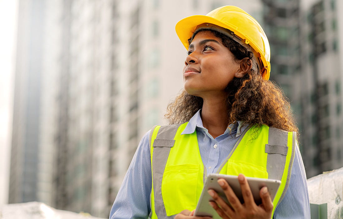 Construction worker in a safety vest and hardhat standing outside of a building.