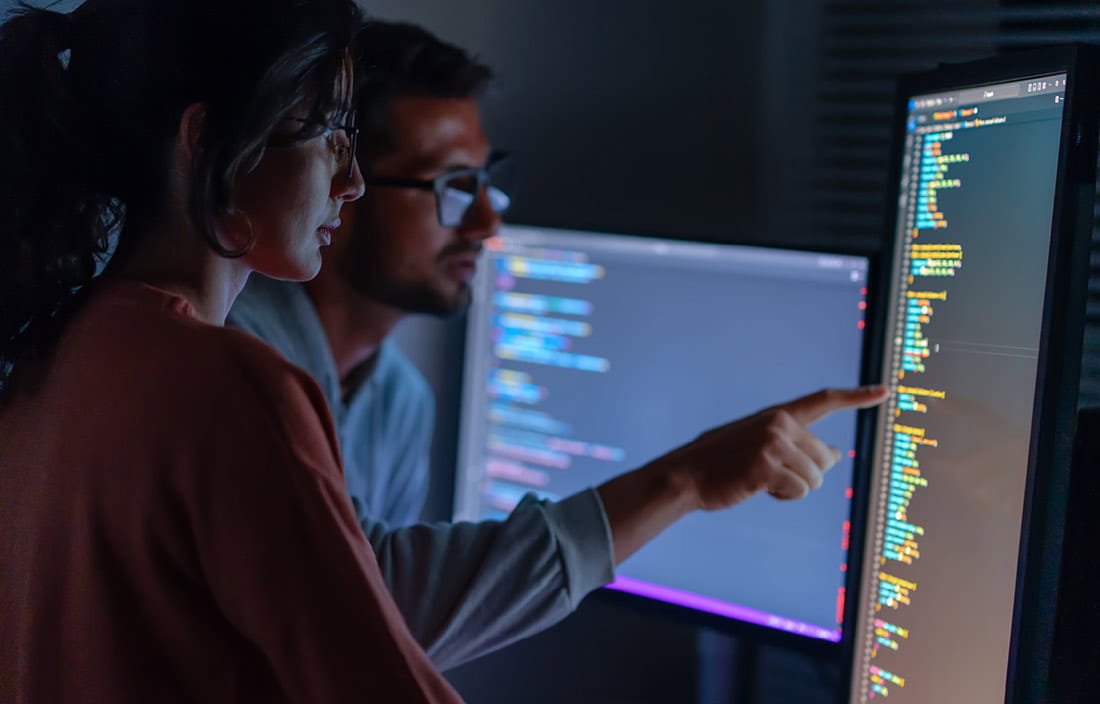 Cybersecurity professionals reading lines of code on their computer screen.