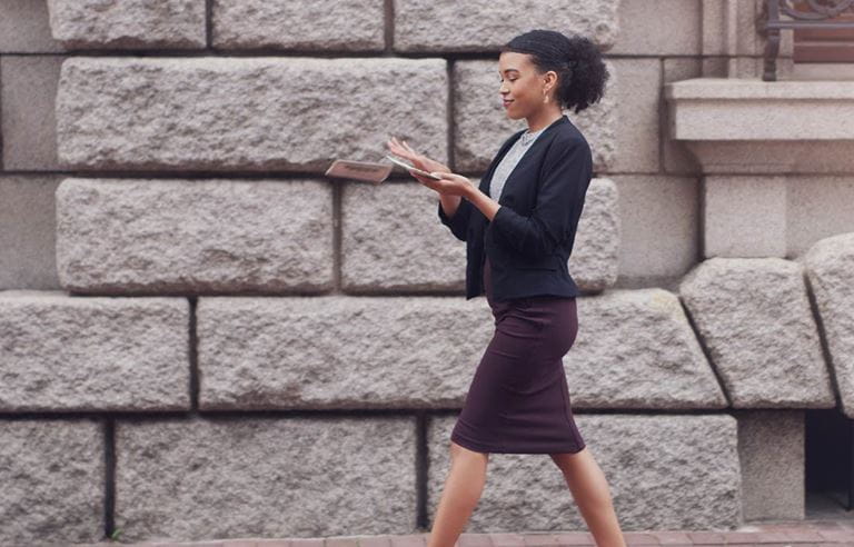 Mortgage banking professional walking while reading an article on their phone.