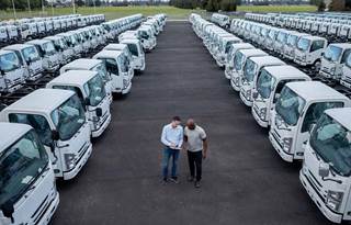 Two workers stand in a lot next to a fleet of trucks