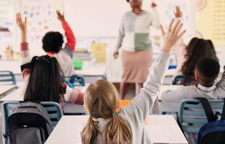 Kids raising their hands in a classroom.