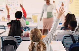 Kids raising their hands in a classroom.