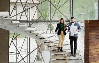 Two civil engineers with blueprints discussing opportunity zones 2.0 while walking down the steps during an office renovation.