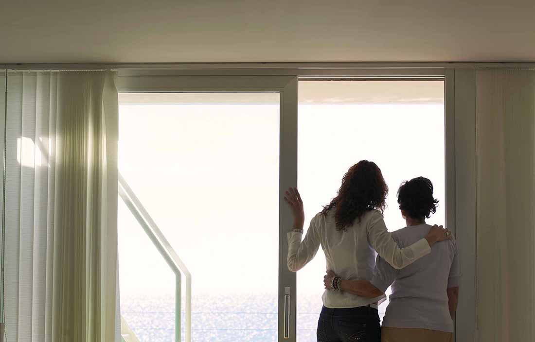 Two family members looking out a window and holding each other.