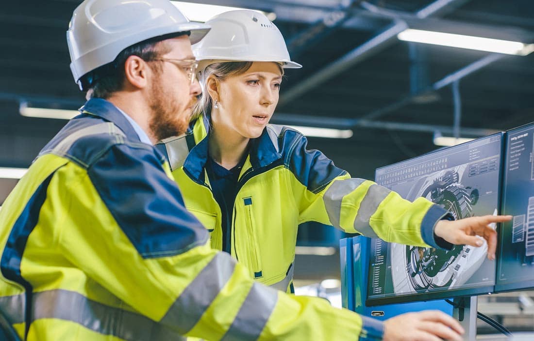 Two manufacturing professionals in hi-vis jackets looking at their computer.