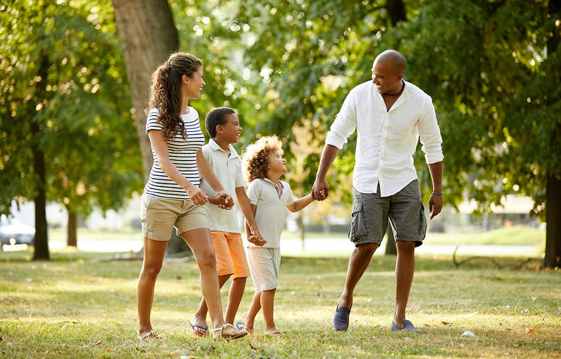 Family holding hands and walking in a park.