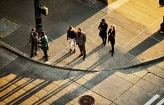 Aerial overview of businesspeople waiting to cross a busy city street.