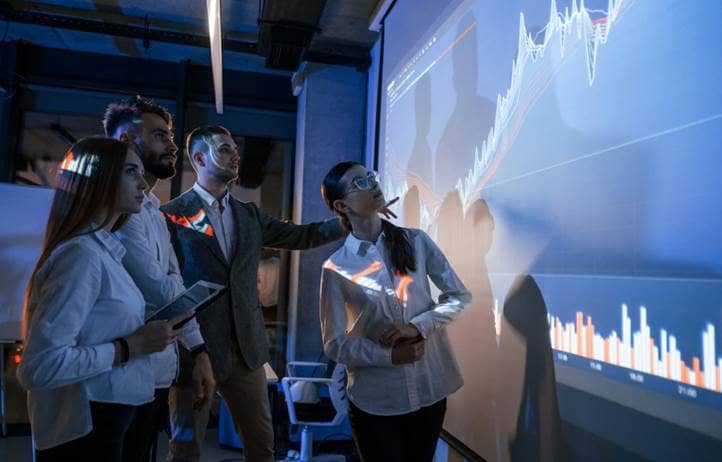 Business professionals looking at a chart on a big screen in front of them.