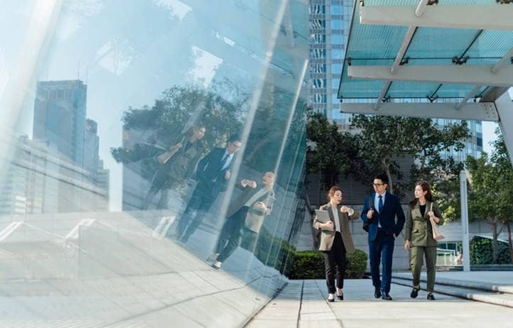 Three business professionals talking while walking outside a modern office building.