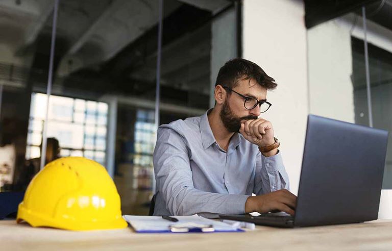 Man working on his laptop with a hard hat next to him on the table