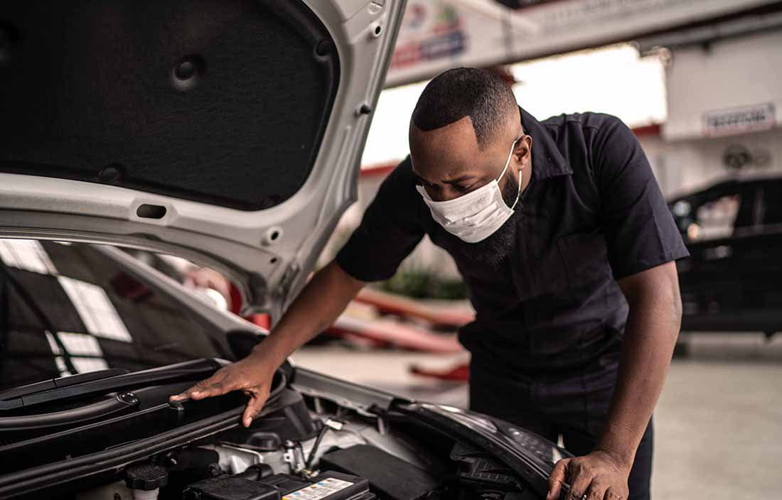 Auto mechanic working on a car while wearing a protective face mask.