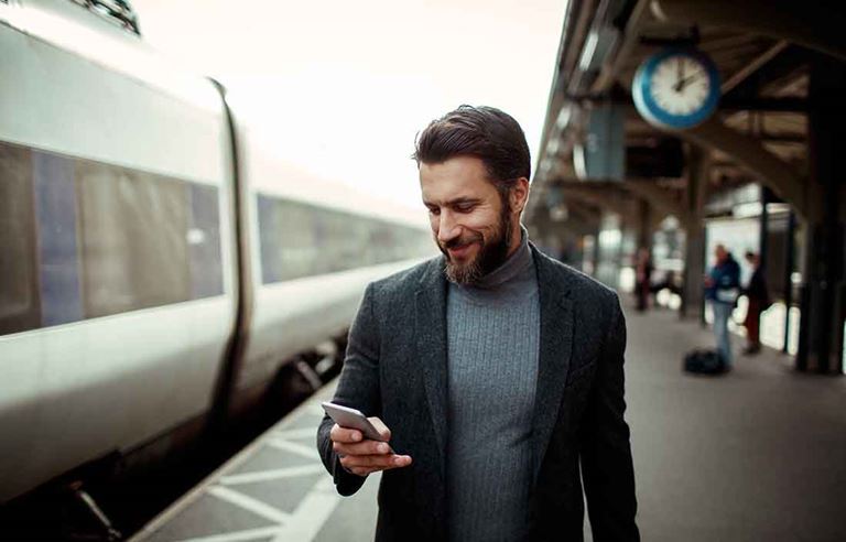 Man walking by train station and looking at his cell phone reading news.