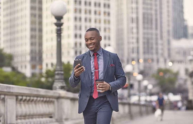 Business professional walking on a bridge while checking their cell phone.