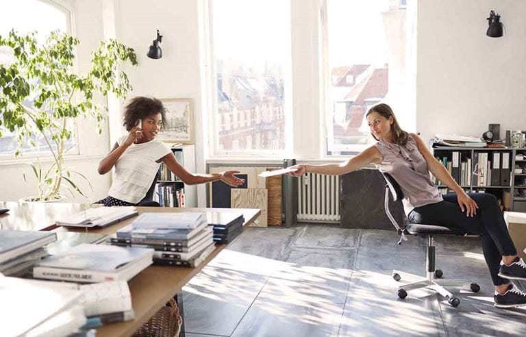 Two business professionals passing paperwork to one another.