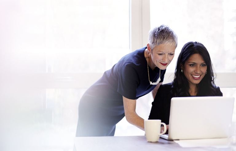 Two businesswomen looking at a laptop in a modern conference room.