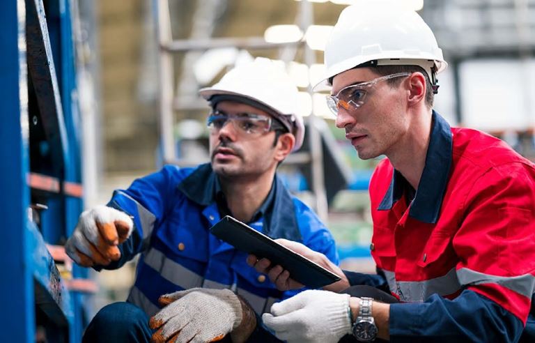 Two automotive workers in hardhats inspecting machinery