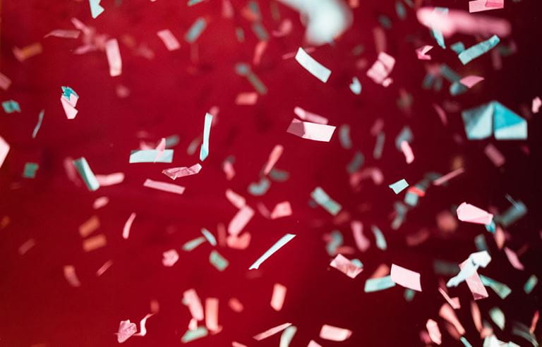 Confetti in the air in front of a red background.