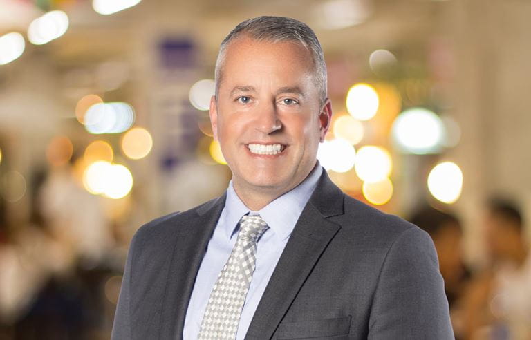 Professional photo of Jason Drake in front of a brightly colored, blurred background.