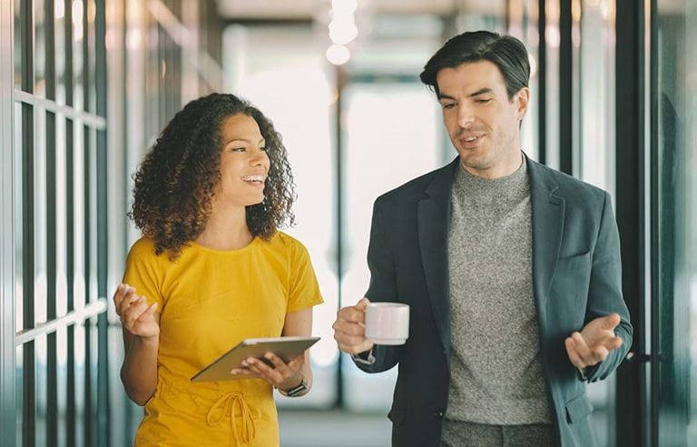 Two business professionals talking and walking down a hallway.