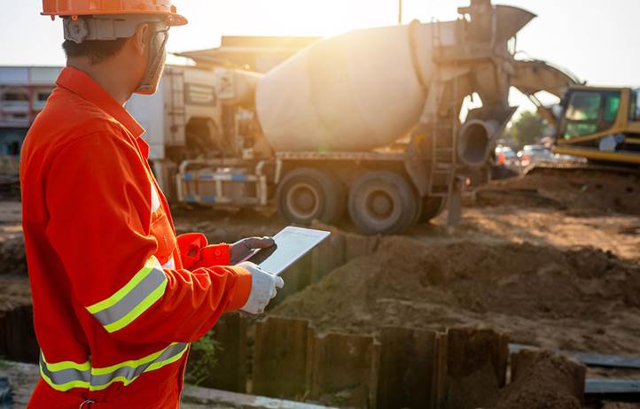 Construction worker holding a clipboard while looking a concrete mixing machine