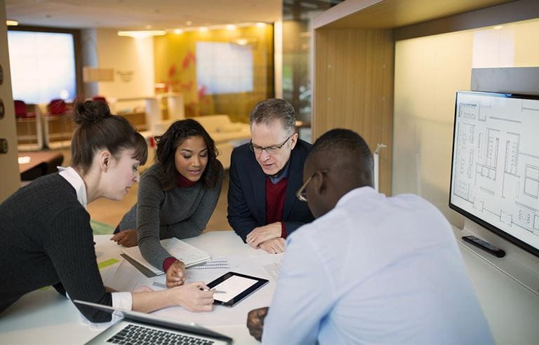 Group of people in an office around a tablet looking at building floor plans