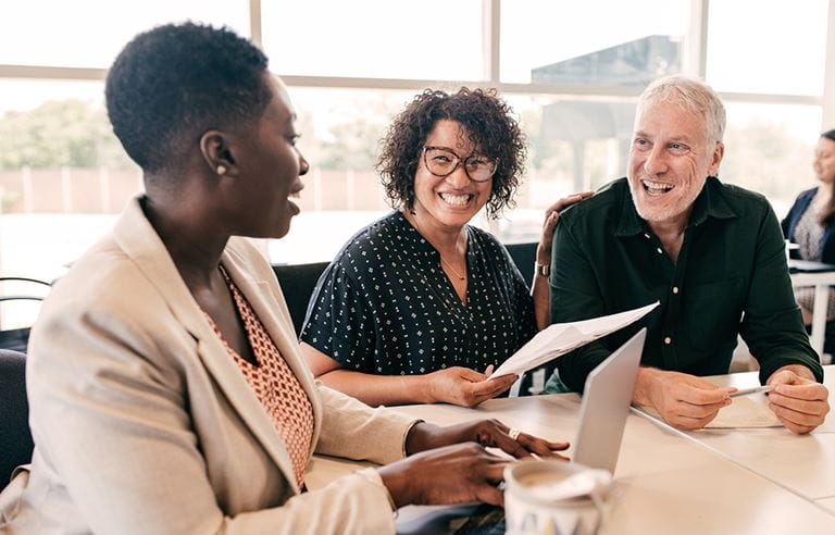 Senior couple moving into senior housing community, talking with a sales rep at a table and laughing