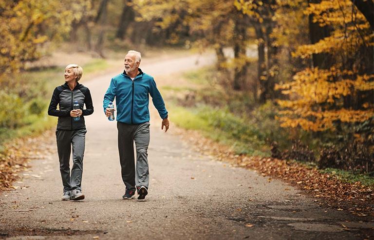 Two active senior adults walking next to a forest in fall