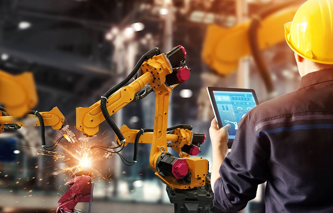 Engineer checking and controlling welding robot in intelligent industrial manufacturing factory