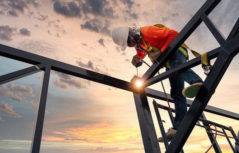 A welder is welding steel on a steel roof truss of an industrial building