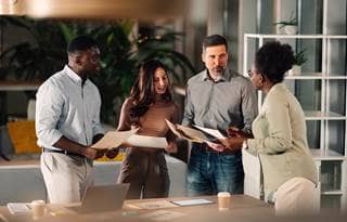 Team of businesspeople in business casual clothes in a modern office building looking at papers while standing around a table