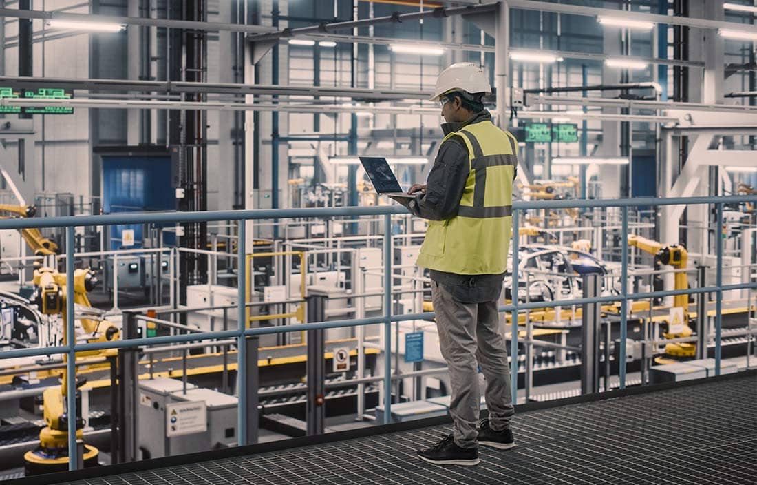 Manufacturing worker on a laptop by machinery in a factory