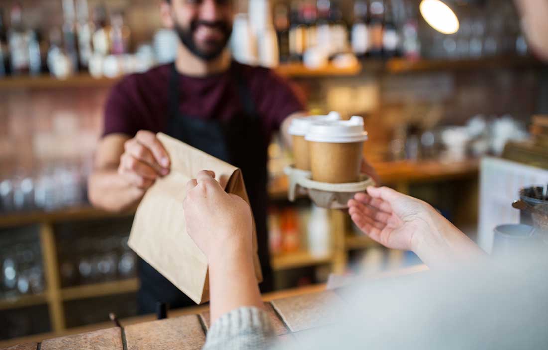 Barista at a cafe handing a customer their coffees and pastries.