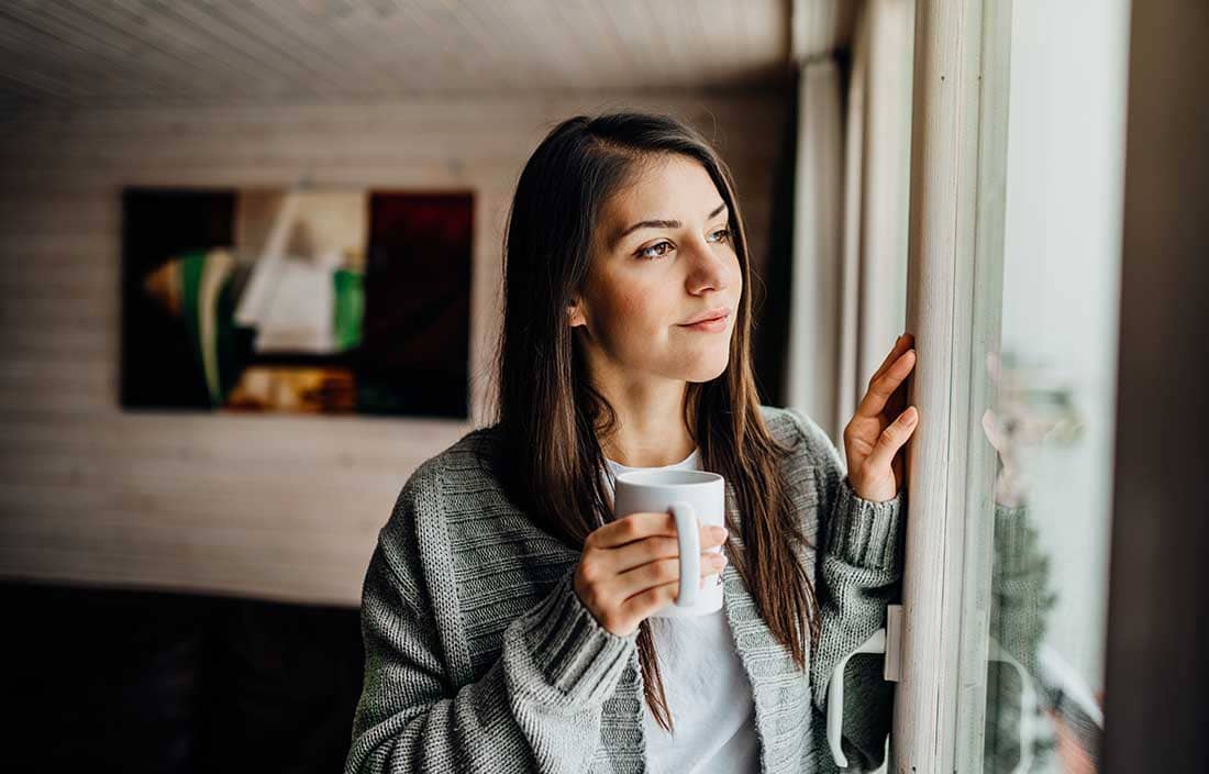 Woman holding a mug and looking out a window.